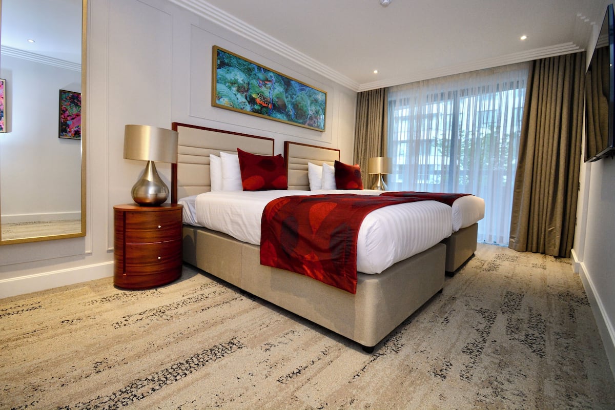 Ruime hotelkamer met een groot bed, een houten nachtkastje, een moderne lamp en een groot raam met gordijnen.