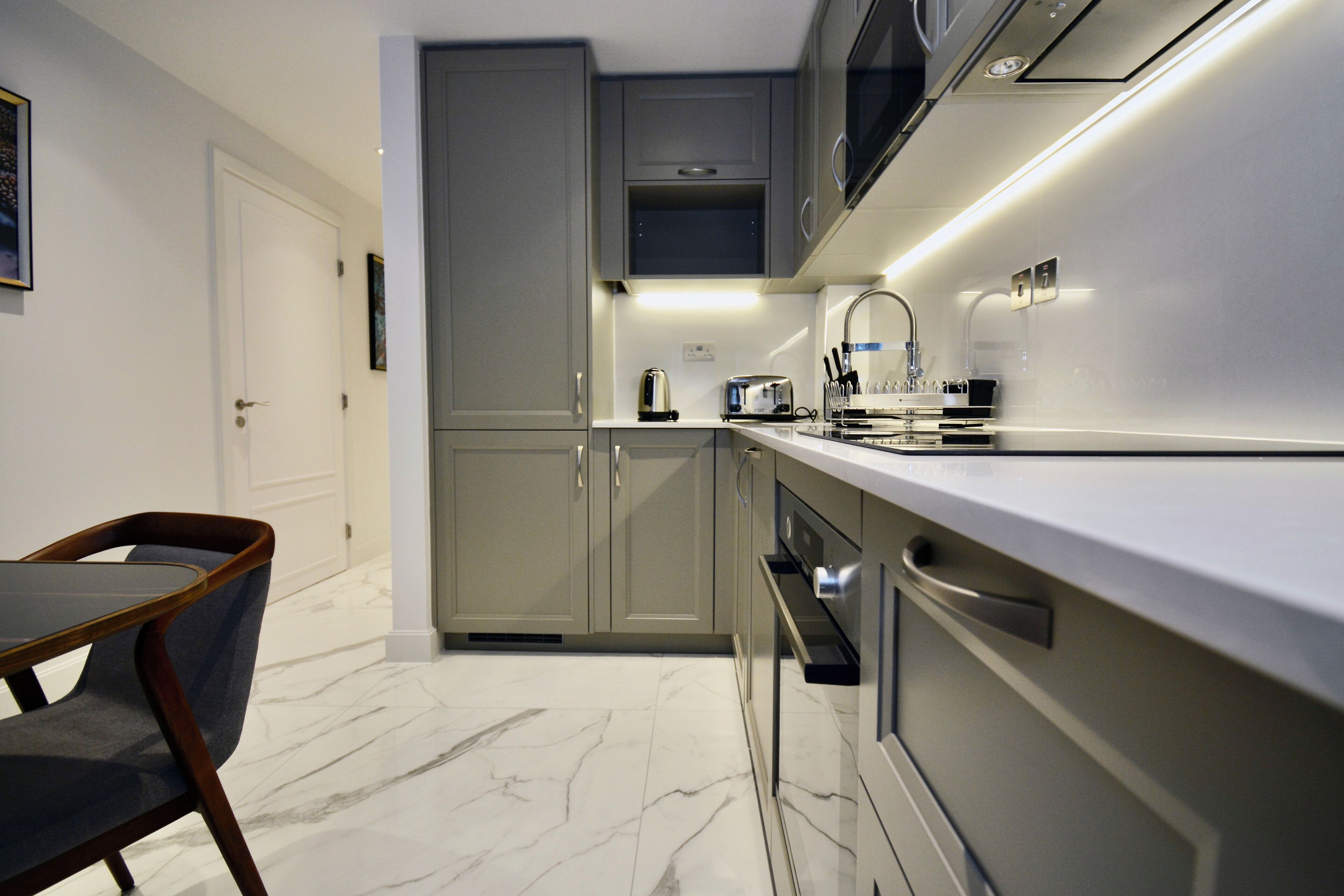 A modern kitchen with grey cabinets, a white countertop, and a marble floor.
