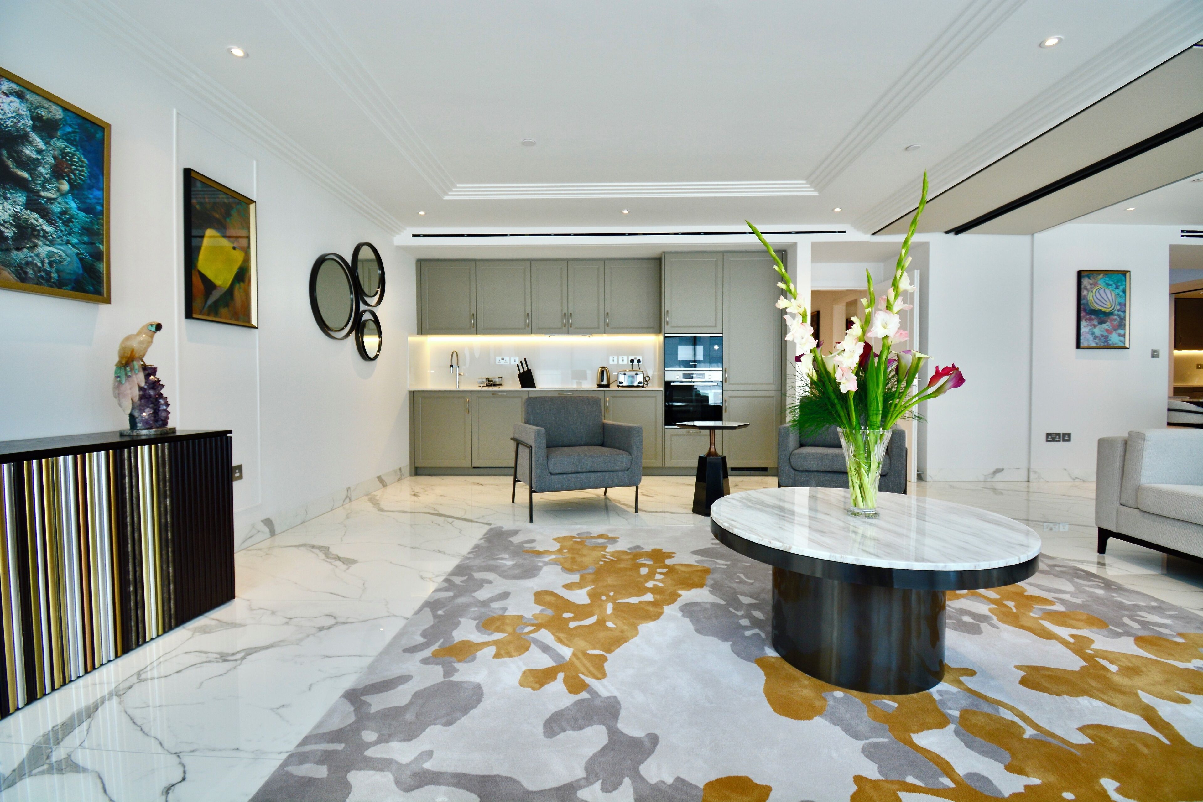 A modern interior with a marble floor, a round coffee table, and a kitchen in the background.