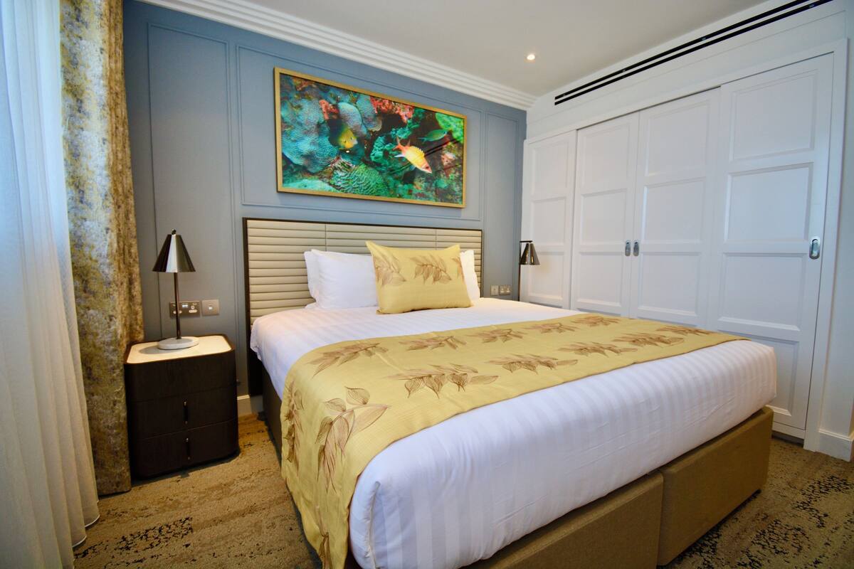 Een hotelkamer met een bed, nachtkastje, lamp, schilderij en een kledingkast.