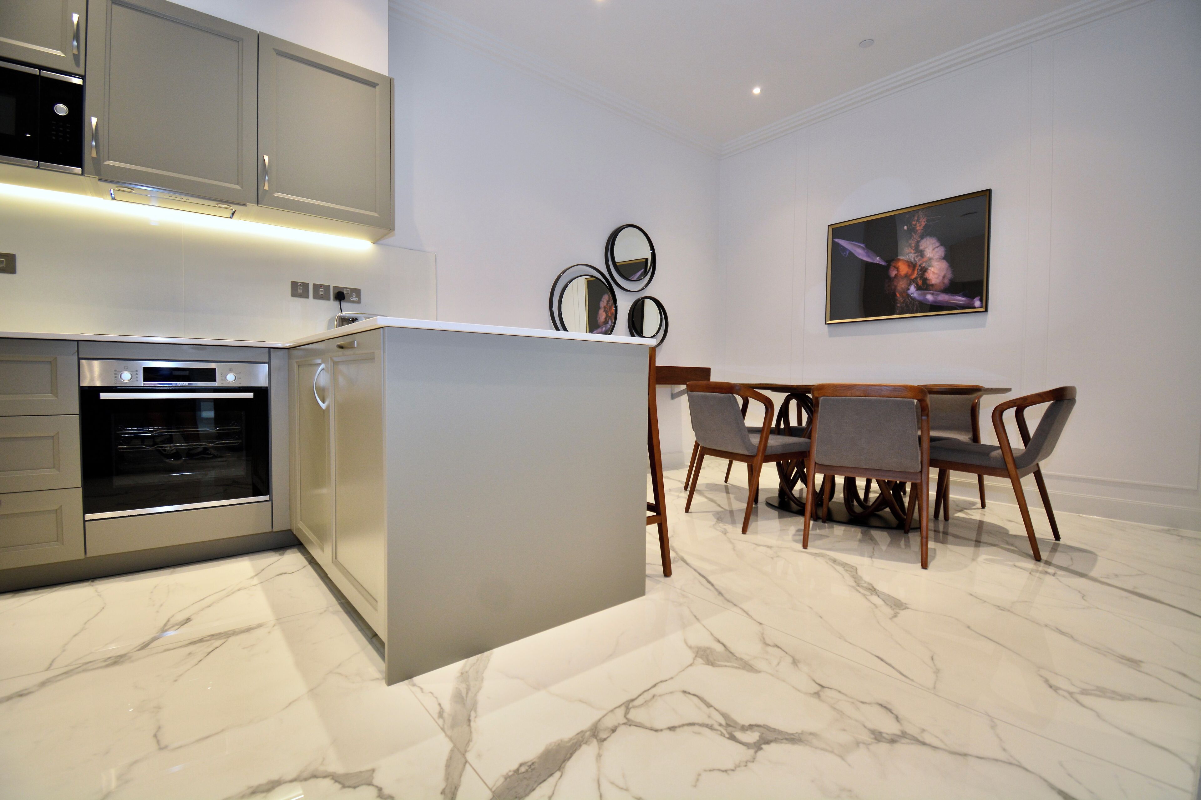A modern kitchen with built-in appliances, a marble floor, and a dining area with a table and chairs.