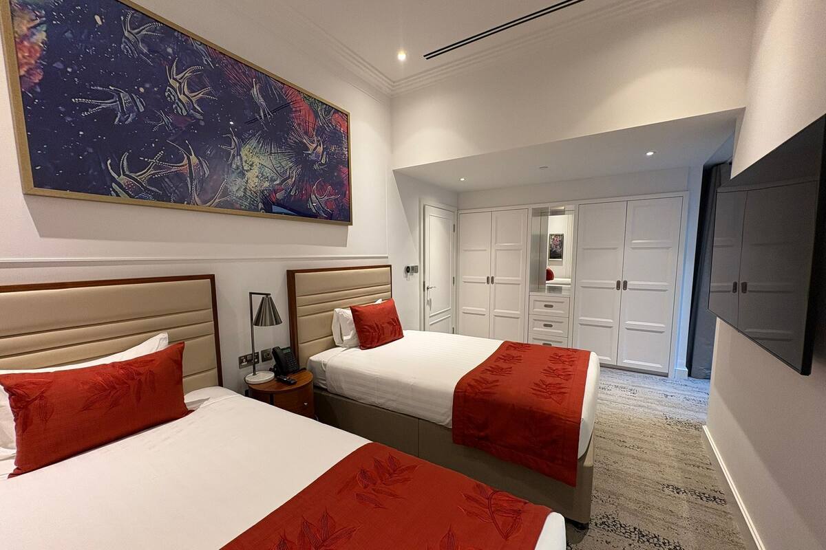 Een hotelkamer met twee bedden, een groot abstract schilderij, een kledingkast en een spiegel.