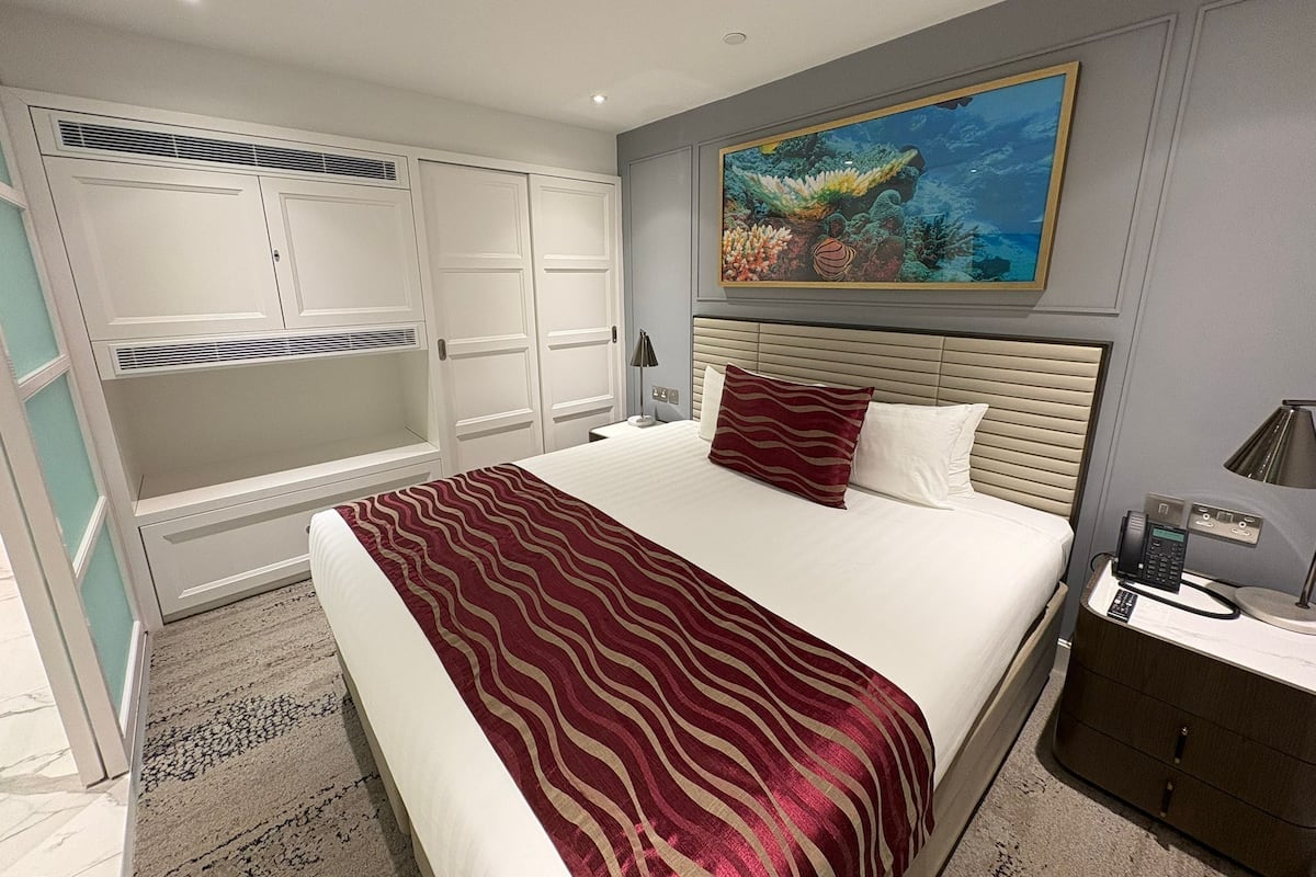 Een hotelkamer met een groot bed, een kledingkast, een bureau en een schilderij van een koraalrif.