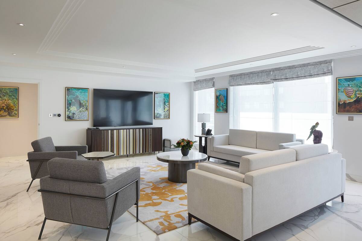 Een moderne woonkamer met een flatscreen televisie, grijze banken, een bijzettafeltje en kunst aan de muren.