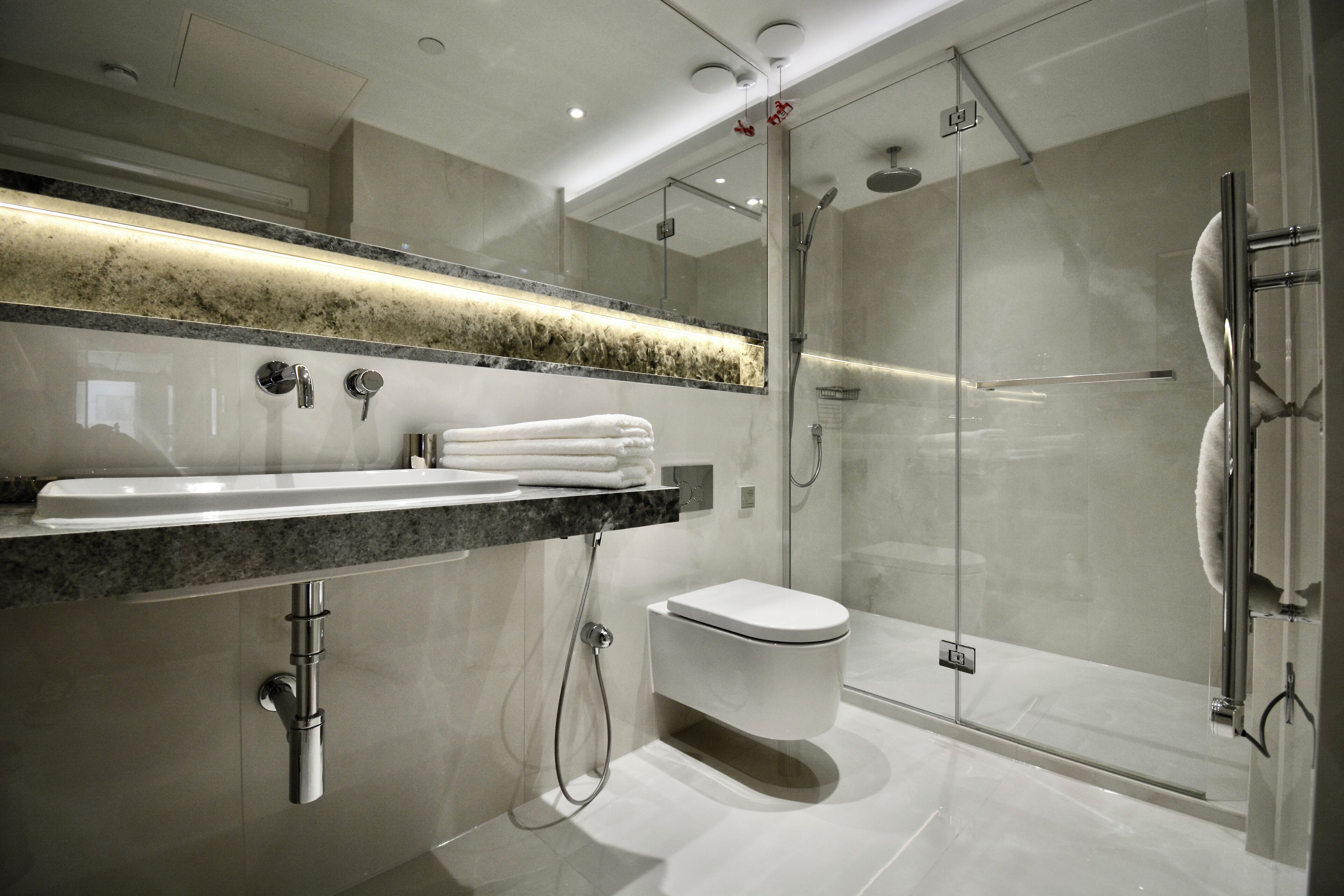 A modern bathroom with a glass shower enclosure, a marble countertop, and a toilet.