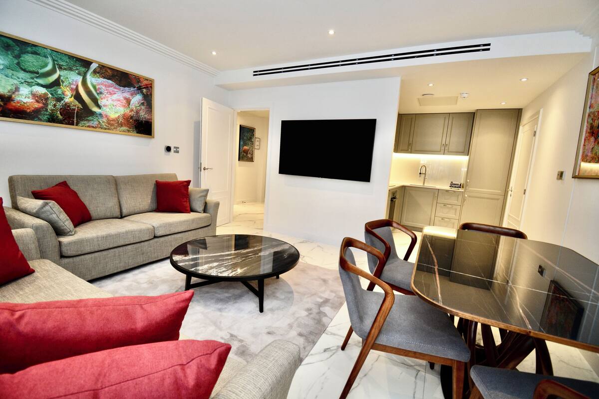 Een moderne woonkamer met een bank, rode kussens, een glazen salontafel en een eethoek met een glazen tafel en stoelen.