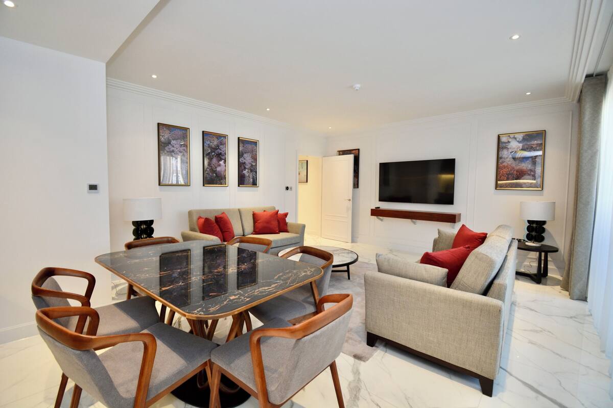 Een moderne woonkamer met een eettafel, banken en een flatscreen televisie aan de muur.