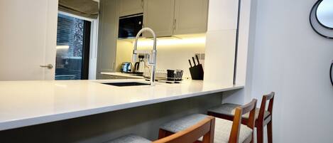 A modern kitchen with a white countertop, wooden chairs, and a built-in oven.