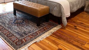 Un dormitorio con cama, un banco, ventilador de techo, alfombra y cuadros en la pared.