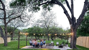 Un patio al aire libre con luces colgantes, asientos y una parrilla.