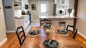 Una cocina moderna con armarios blancos, una isla central y un comedor con mesa y sillas de madera.