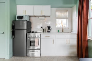 A kitchen with white cabinets, stainless steel appliances, a window with blinds, and a red curtain.