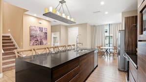 A modern kitchen with a large island, wooden cabinets, and a stainless steel refrigerator. - 3045 MagicVillage 8 guests 6 min Disney near 192 (Kissimmee)