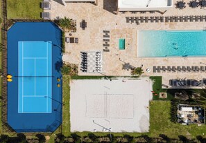 An aerial view of a property with a tennis court, a swimming pool, and outdoor seating areas.