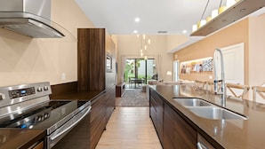 A modern kitchen with a stainless steel stove, a double sink, and wooden cabinetry. - 3045 MagicVillage 8 guests 6 min Disney near 192 (Kissimmee)