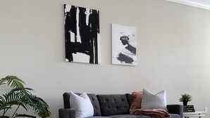 Un soggiorno moderno con un divano grigio, due tavolini, un tavolino da caffè e opere d'arte astratte alle pareti.
