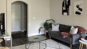 Un soggiorno moderno con un divano grigio, un tavolino da caffè e una ventola a soffitto. Si apre una porta verso un'altra stanza e c'è una pianta nell'angolo.