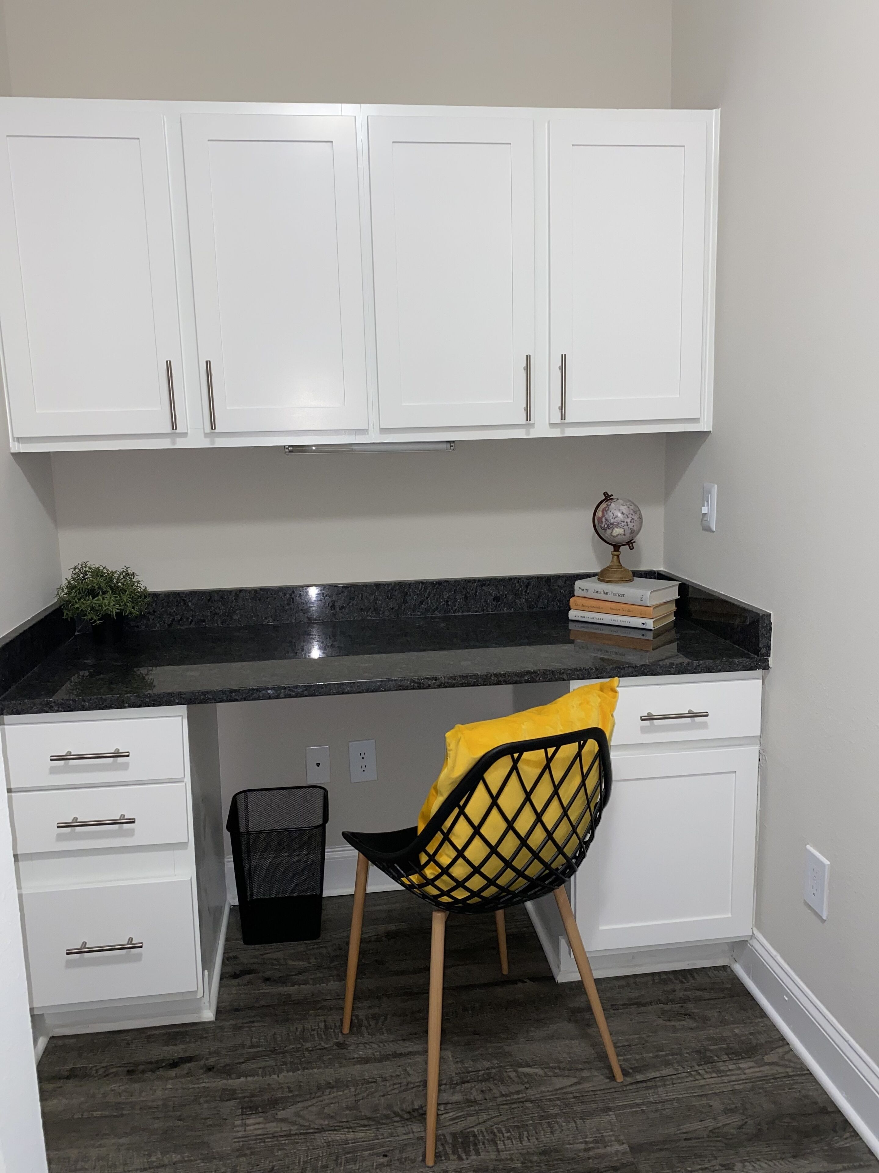 Una cocina con armarios blancos, encimera negra, una silla con cojín amarillo y un globo terráqueo sobre la encimera.