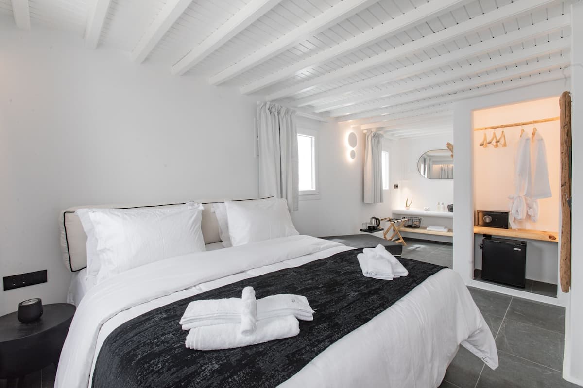 Une chambre d’hôtel moderne dotée d’un grand lit, d’une table de chevet, d’un miroir et d’une salle de bain avec un lavabo et un porte-serviettes.