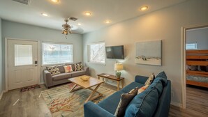 A living room with a sofa, a coffee table, a TV, and a painting on the wall. - Amazing bay views from this 4 bedroom 4 bath house (Port Aransas)