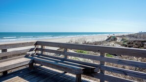 A wooden bench overlooking a beach with a clear view of the ocean and distant buildings. - Amazing bay views from this 4 bedroom 4 bath house (Port Aransas)