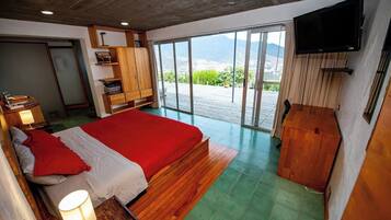 A bedroom with a large bed, a television, and a sliding glass door leading to a balcony with a view of the outdoors.