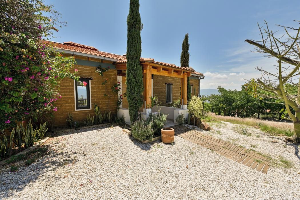 A two-story house with a tiled roof, a gravel driveway, and a variety of plants and trees.