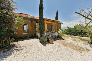 Una casa de dues plantes amb teulada de rajola, carril d'accés de grava i una varietat de plantes i arbres.