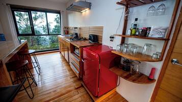 Een kleine keuken met houten vloeren, een rode koelkast en een bargedeelte met krukken.