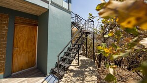 A modern building with a wooden door, a staircase leading to a balcony, and a view of trees and a clear sky. - A beautiful loft in nature but close to the city, with pool /streamer (Oaxaca de Juarez)
