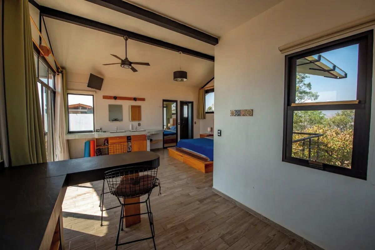A spacious room with a large window, a ceiling fan, and a bed with a blue bedspread.