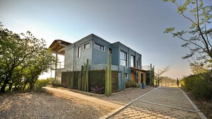 Una casa moderna de dos pisos con fachada azul, camino de grava y sendero hexagonal de ladrillo que conduce a la entrada.
