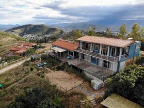 Una casa moderna de dos pisos con balcón, rodeada por un paisaje montañoso.