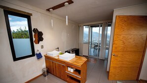 Un baño moderno con tocador de madera, dos lavamanos y vistas a la ciudad a través de grandes ventanales.