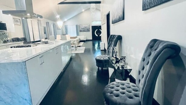 A modern kitchen with a central island, a dining area with a high chair, and a large painting on the wall. - Elegant NW Atlanta Oasis, 2 Kitchens, Sauna, Billiards, Patio, Sundeck & Yard! (Atlanta)