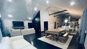 A modern living room with a large white sofa, a wooden dining table with benches, and a herringbone-patterned rug. - Elegant NW Atlanta Oasis, 2 Kitchens, Sauna, Billiards, Patio, Sundeck & Yard! (Atlanta)