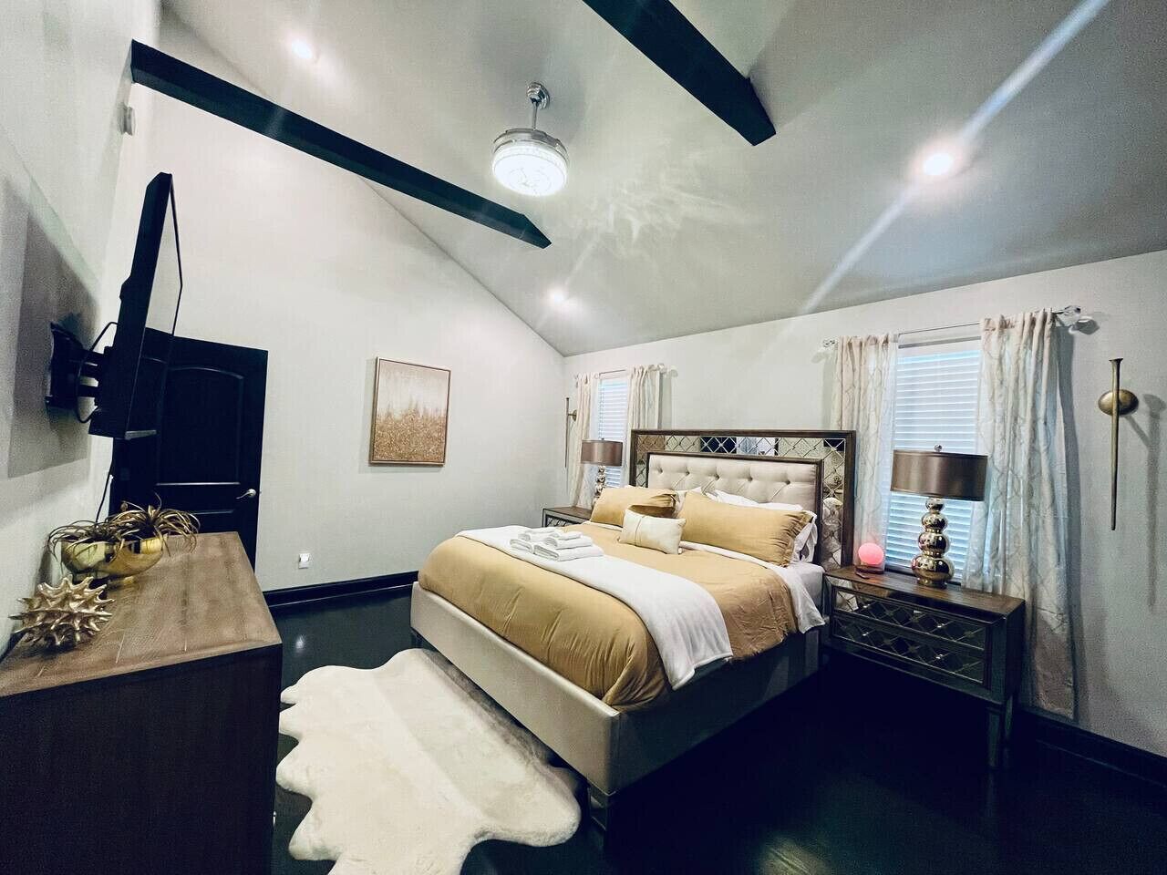 A bedroom with a bed, bedside tables, a desk, a television, and a ceiling light fixture.