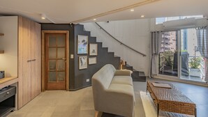 Ein modernes Wohnzimmer mit einer Couch, einem Holzkabinett, einer Treppe und einem großen Fenster mit Blick auf Gebäude.