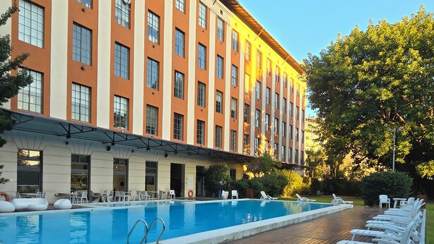 Un hotel con piscina, terraza de madera y sillones de descanso.