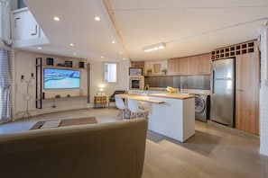 Une cuisine moderne dotée d’un îlot central, d’appareils électroménagers intégrés et d’un téléviseur à écran plat fixé au mur.