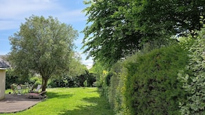A house with a sloped roof, a wooden deck, and a garden with a large tree and various shrubs.