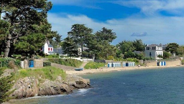 A coastal property with a stone wall, a beach, and several houses with blue doors.