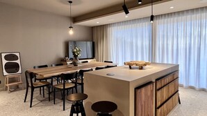 A modern dining area with a wooden table and chairs, a central island with stools, and a television on the wall.