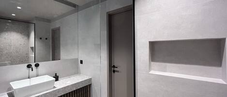 Une salle de bain moderne avec un grand miroir, un lavabo rectangulaire et un espace douche.