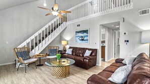 A spacious living room with a high ceiling, a staircase, a brown leather sofa, a glass coffee table, and a wicker chair. - Perfect location Walk to the village and beach Private Balcony Heated Pool (Siesta Key)