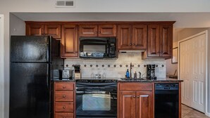 Eine Küche mit Holzausstattung, einem schwarzen Kühlschrank, einer Mikrowelle, einem Backofen und einem Geschirrspüler.