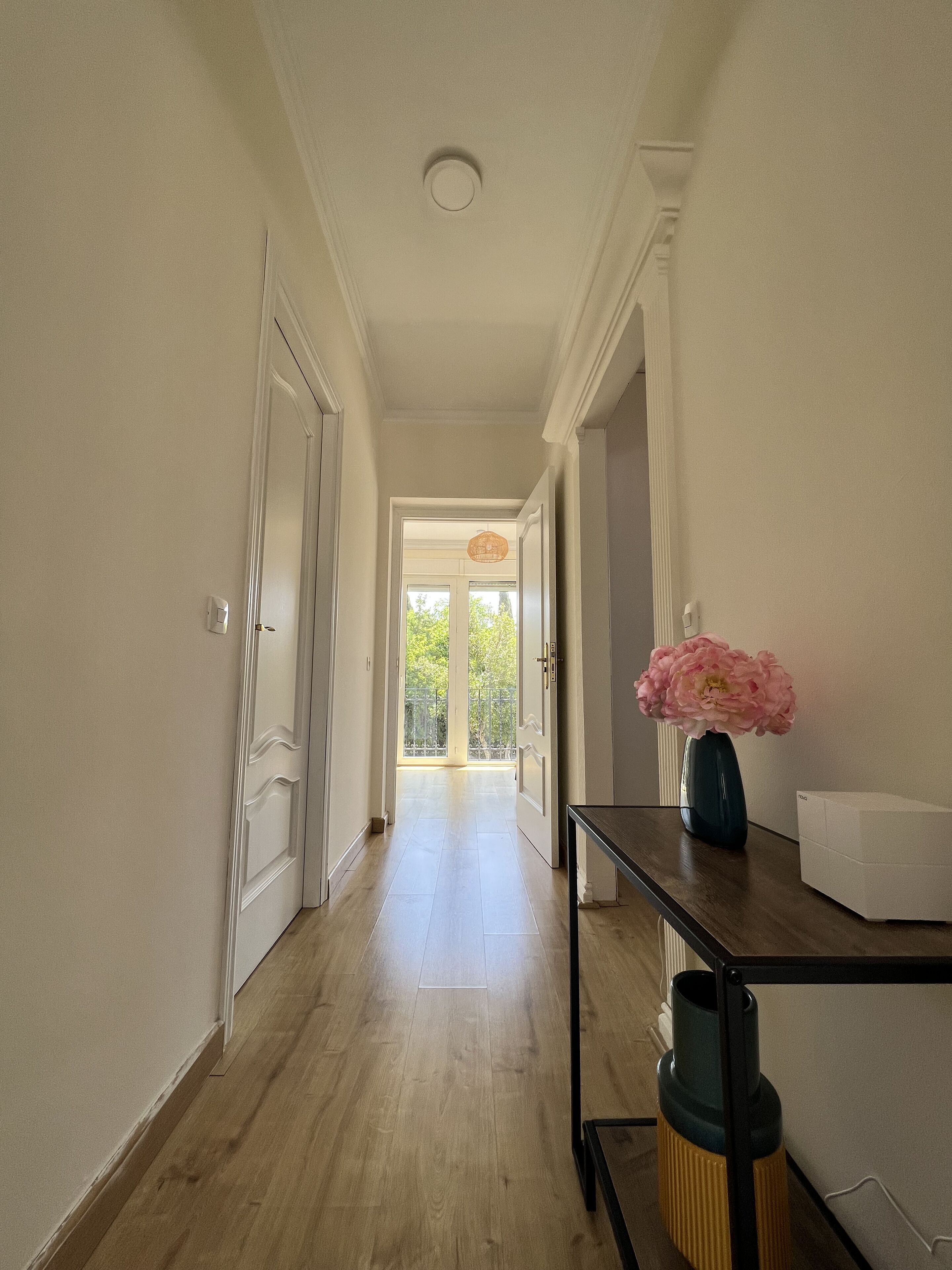 Un pasillo con suelo de madera, paredes blancas y una puerta que da a un balcón.