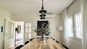 Un comedor con mesa de madera, sillas, un jarrón con flores, una lámpara en el techo y una ventana con cortinas.