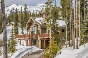 A lodge with a wooden exterior, large windows, and a balcony overlooking a snowy landscape with mountains in the background. - Spacious Ski-In/Ski-Out Retreat (Big Sky)