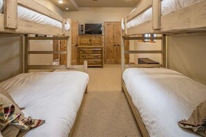 A bunk bed room with two beds, a television on a wooden cabinet, and a carpeted floor. - Spacious Ski-In/Ski-Out Retreat (Big Sky)